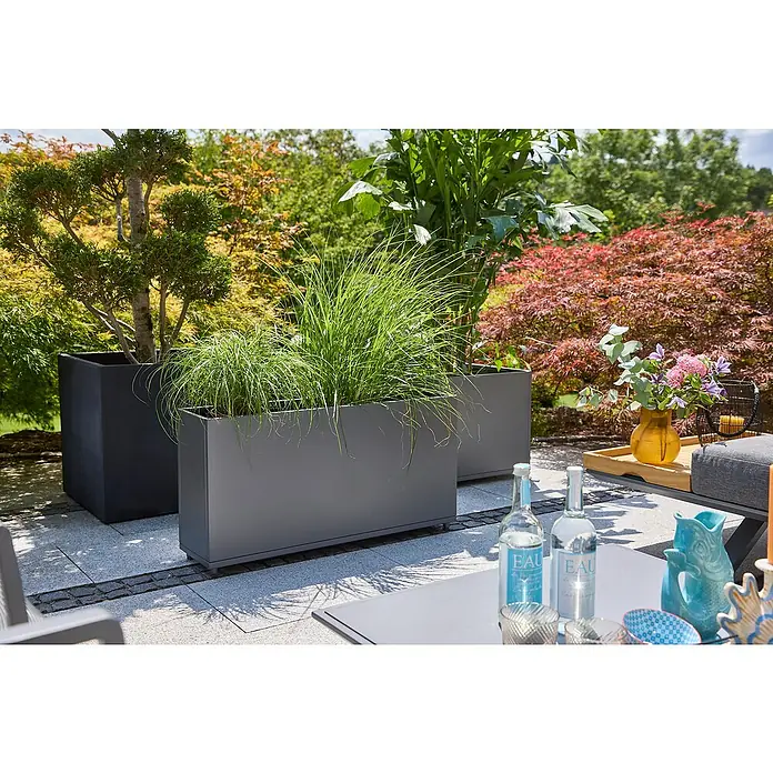 Sunfun Lumar Pflanzkübel eckig - Außenmaß (L x B x H): 50 x 50 x 45 cm, Stahl, Night-Grey - Eine Nahaufnahme von rechteckigen Pflanzgefäßen in verschiedenen Größen, die mit Gräsern und Bäumen bepflanzt sind und im Freien stehen.