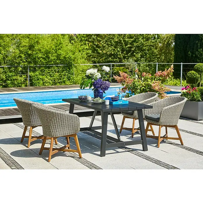Sunfun Pauline Gartensessel - B x T x H: 62 x 70 x 80 cm, Polyrattan, Akazie, Bambus Grey/Naturbraun - Ein grauer Gartentisch mit vier Stühlen aus Rattan und hellbraunen Beinen steht auf einer gepflasterten Terrasse mit Pool im Hintergrund.