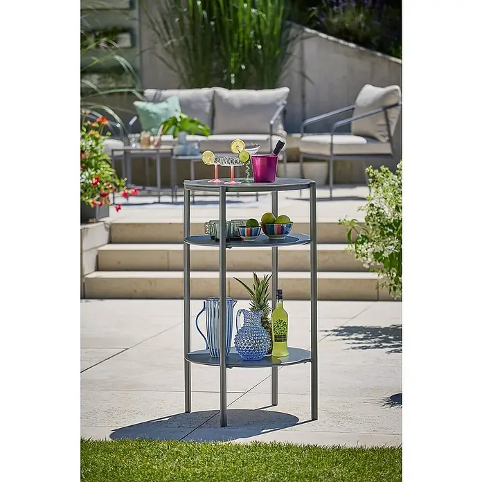 Sunfun Solo Garten-Beistelltisch rund - Ø x H: 65 x 108 cm, Stahl, Night-Grey - Ein grauer, dreistöckiger Servierwagen mit Getränken und Deko-Elementen steht auf einer Terrasse.