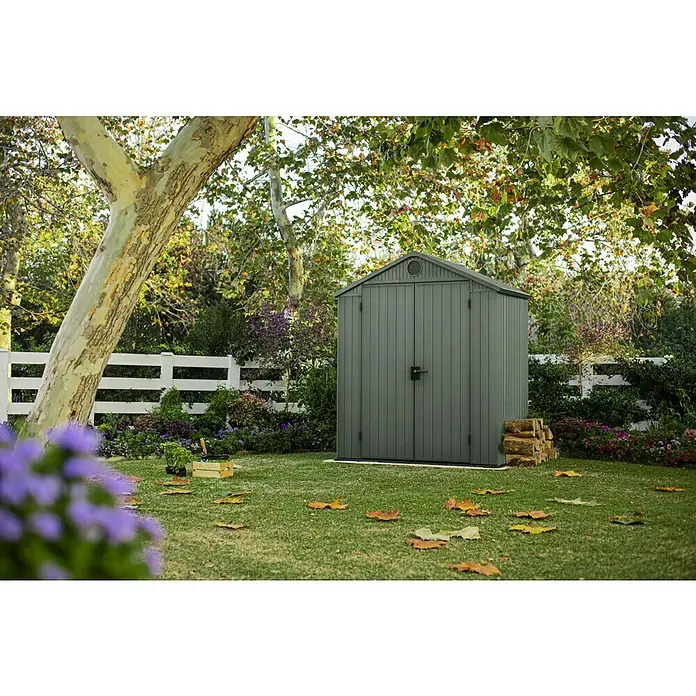 Keter Gartenhaus Darwin 6x4 - Außenmaß inkl. Dachüberstand (B x T): 190 x 122 cm, Kunststoff, Grün, 2,3 m² - Ein graues Gartenhaus steht auf einem grünen Rasen, umgeben von Bäumen und Blumen. Es ist perfekt für die Aufbewahrung von Gartengeräten.