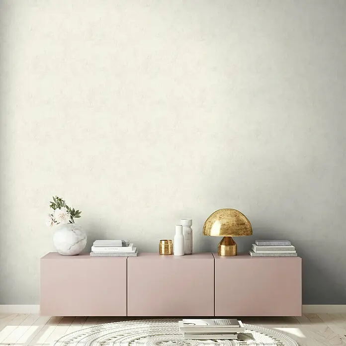 A.S. Création New Walls Vliestapete Textil - Creme, Uni, 10,05 x 0,53 m - Interior mit einem rosa Schrank, dekoriert mit einer goldenen Lampe, Büchern und Blumen, vor einer getäfelten Wand für eine ruhige Atmosphäre.