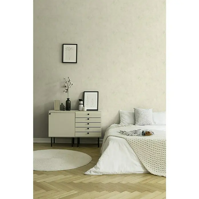 A.S. Création New Walls Vliestapete - Creme, Uni, 10,05 x 0,53 m - Schlafzimmer Interieur mit einer weißen Kommode, einem runden Teppich und einem dekorierten Bett mit Kissen und einer Tagesdecke.