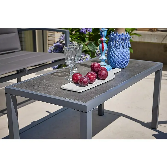 Loungemöbel-Set - 4 -tlg., Metall/Textil, Schwarz/Grau - Nahaufnahme eines grauen Couchtischs mit Pflaumen, Gläsern und dekorativen Vasen auf einer Terrasse.