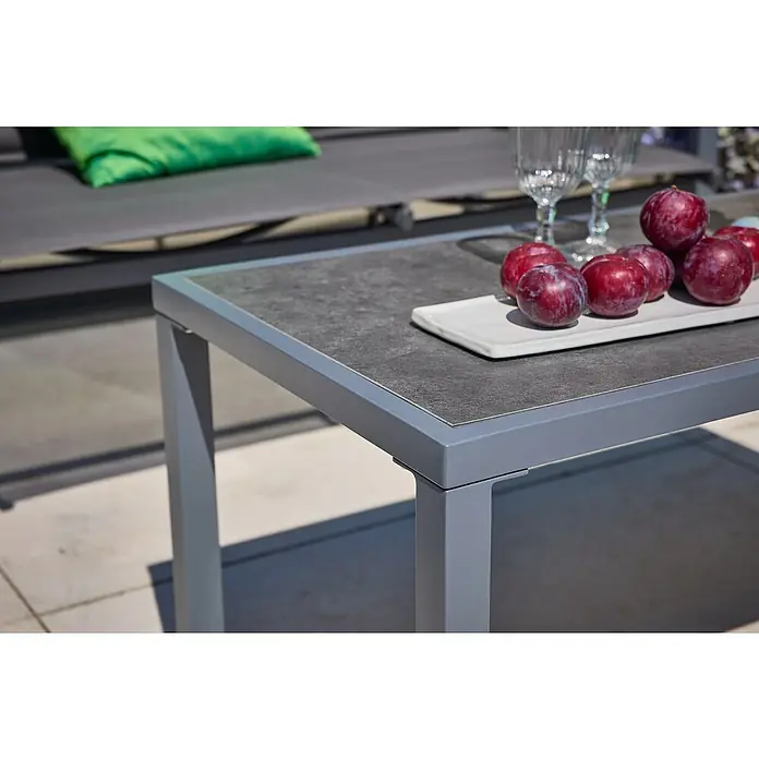 Loungemöbel-Set - 4 -tlg., Metall/Textil, Schwarz/Grau - Nahaufnahme eines modernen Gartentisches mit Steinplatte, auf dem Pflaumen auf einem Teller liegen.