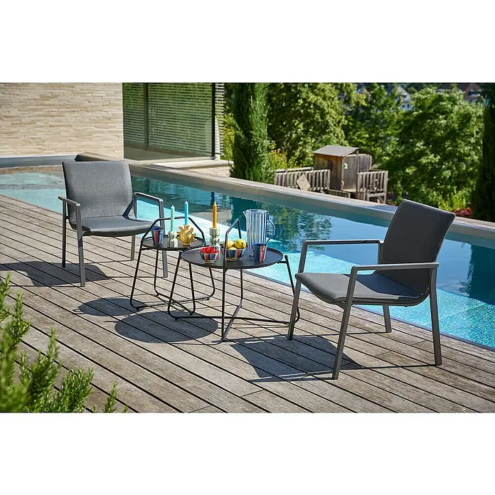 Sunfun Melina Garten-Beistelltisch rund - Ø x H: 80 x 60,5 cm, Stahl, Night-Grey - Zwei graue Sessel und ein kleiner Tisch stehen auf einer Holzterrasse neben einem Pool. Dekorative Accessoires schmücken den Tisch.