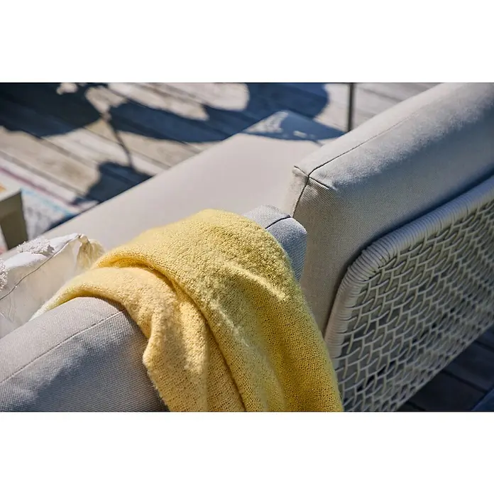 Sunfun Solo Rope Sofá de conjunto - An x Pr x Al: 167,5 x 86,5 x 66 cm - Primer plano de un sofá de exterior con una manta amarilla y un cojín blanco sobre una terraza de madera. El sofá tiene un respaldo de mimbre claro.