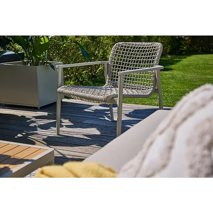 Sunfun Solo Rope Loungesessel - B x T x H: 69,5 x 74 x 72 cm, Aluminium, Kunststoff, Light-Greige - Nahaufnahme eines modernen Sessels mit Armlehnen und geflochtener Sitzfläche auf einer Holzterrasse mit Grün im Hintergrund.