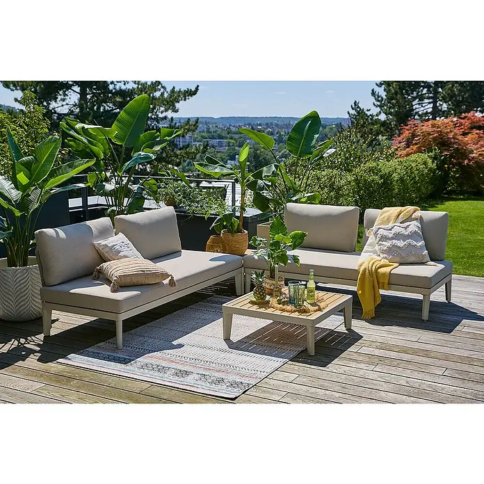 Sunfun Solo Conjunto de muebles sofá + mesa de centro - 4 pzs., Gris claro - Un elegante conjunto de muebles de jardín con cojines beige y una mesa a juego, rodeado de exuberantes plantas en una terraza de madera.