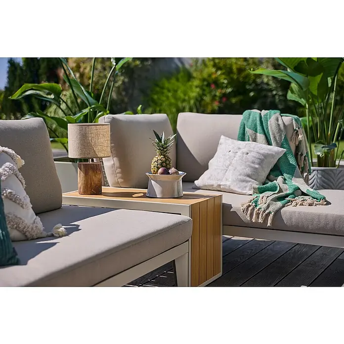 Sunfun Solo Garten-Beistelltisch - L x B x H: 73 x 38,5 x 41 cm, Aluminium, Light-Greige - Ein stilvolles Outdoor-Sofa mit Beistelltisch, Lampe und dekorativen Elementen wie Kissen und einer Ananas in einer Schale.