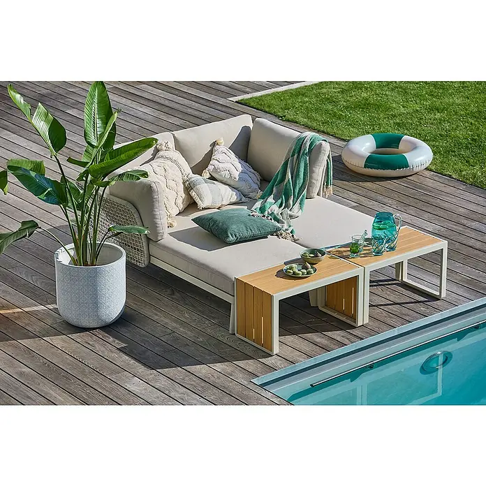 Sunfun Solo Conjunto de muebles chaise lounge + mesa auxiliar - 4 pzs., Gris claro - Rincón de jardín acogedor con sofá beige, cojines decorativos, mesas auxiliares y una gran maceta con planta verde.