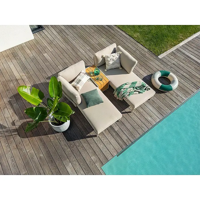 Sunfun Solo Conjunto de muebles chaise lounge + mesa auxiliar - 3 pzs., Gris claro - Un elegante conjunto de salón hecho de tela beige con cojines decorativos y una mesa de café en una cubierta de madera al lado de una piscina.