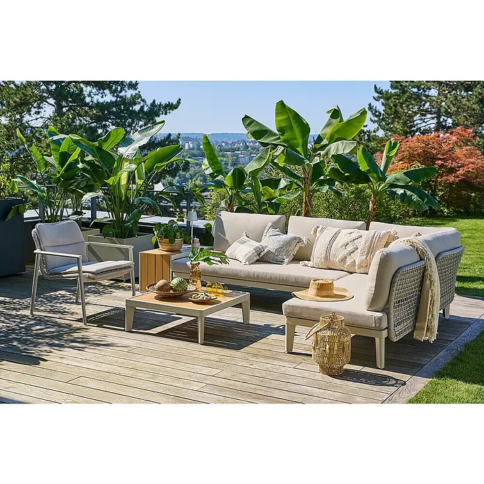 Sunfun Loungemöbel-Set Solo Rope X - 7 -tlg., Aluminium/Polyrattan/Olefin, Light-Greige - Eine entspannende Gartenszene mit einem grauen Loungesofa, einem Couchtisch und einem Sessel auf einer hölzernen Terrasse, umgeben von üppigem Grün.