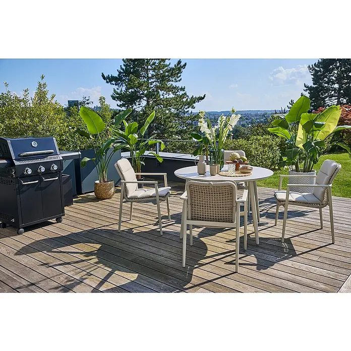 Kingstone Gasgrill Diner 3000 Beast - Grillfläche (B x T): 63,7 x 43 cm, 10,5 kW, Anzahl Brenner: 3 Stk. - Eine Gartenszene mit einem runden Tisch und Stühlen auf einer Holzterrasse, neben einem Grill und üppigem Grün, ideal für Mahlzeiten im Freien.
