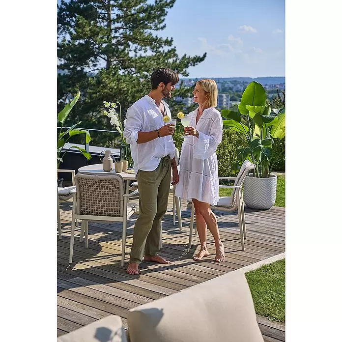 Macetero redondo Birmingham - Dimensiones externas (Ø x Al): 40 x 40 cm, Material compuesto, Crema - Dos personas se relajan en un patio con sillas de exterior trenzadas, una mesa a juego y una gran maceta. El mobiliario es de color claro y acogedor.