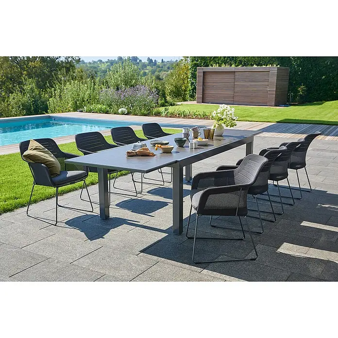 Sunfun Gartenmöbel-Set Maja - 9 -tlg., Night-Grey, Ausziehbar, Tisch (L x B x H): 200-300 x 100 x 74 cm, Stuhl (B x T x H): 57 x 65 x 83 cm - Ein grauer Esstisch mit passenden Stühlen auf einer Terrasse. Der Tisch ist mit Geschirr und Blumen dekoriert und bietet Platz für mehrere Personen.