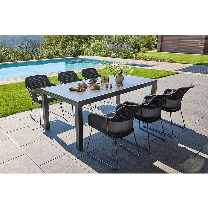 Sunfun Gartenmöbel-Set Maja - 7 -tlg., Night-Grey, Ausziehbar - Ein Gartentisch mit sechs Stühlen steht im Freien, gedeckt mit Geschirr und einer Vase mit Blumen, neben einem Pool. Die Sitzgruppe lädt zum Verweilen ein.