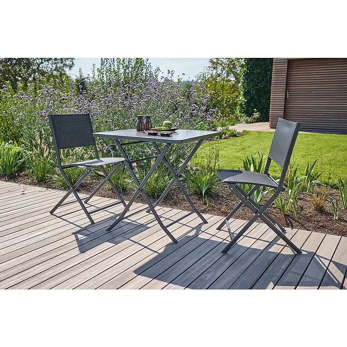 Sunfun Balkonmöbel-Set Maja - 3 -tlg., Night-Grey, Tisch (LxBxH): 70 x 70 x 71 cm, Stuhl (TxBxH): 46 x 52 x 81 cm - Ein graues Gartentischset mit zwei Stühlen steht auf einer Holzterrasse vor einem üppigen Garten. Ideal für entspannte Stunden im Freien.