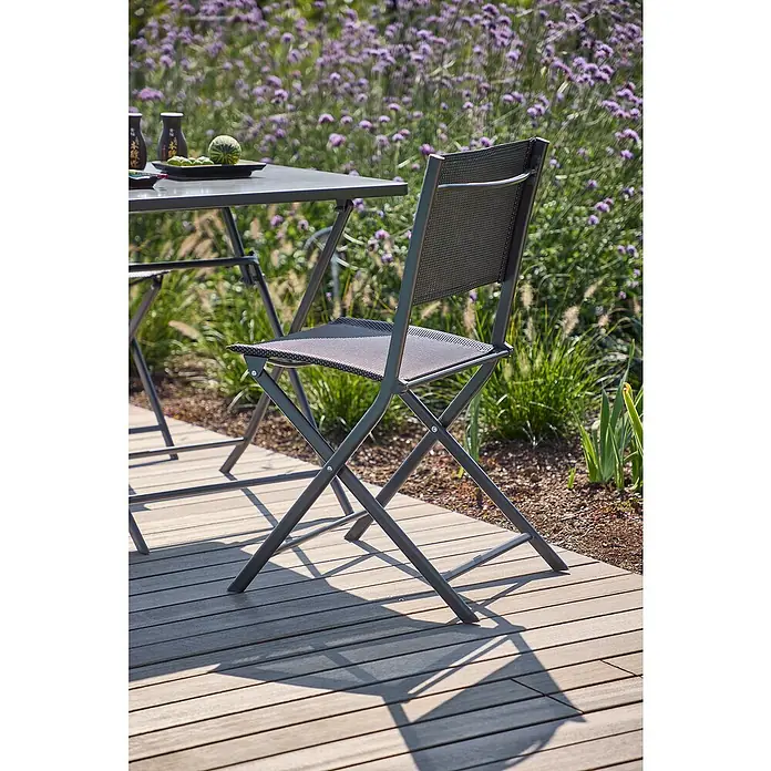 Sunfun Balkonmöbel-Set Maja - 3 -tlg., Night-Grey, Tisch (LxBxH): 70 x 70 x 71 cm, Stuhl (TxBxH): 46 x 52 x 81 cm - Nahaufnahme eines stilvollen, klappbaren Gartenstuhls aus Metall mit Netzmuster auf einer Holzterrasse.