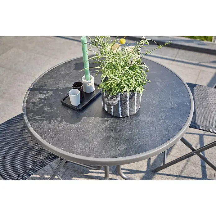MFG Balkontisch rund Boulevard - Ø x H: 70 x 110 cm, Stahl, Mecalit, Klappbar, Anthrazit - Nahaufnahme eines runden Gartentisches mit grauem Rahmen, einer Pflanze, Kerze und Bechern.