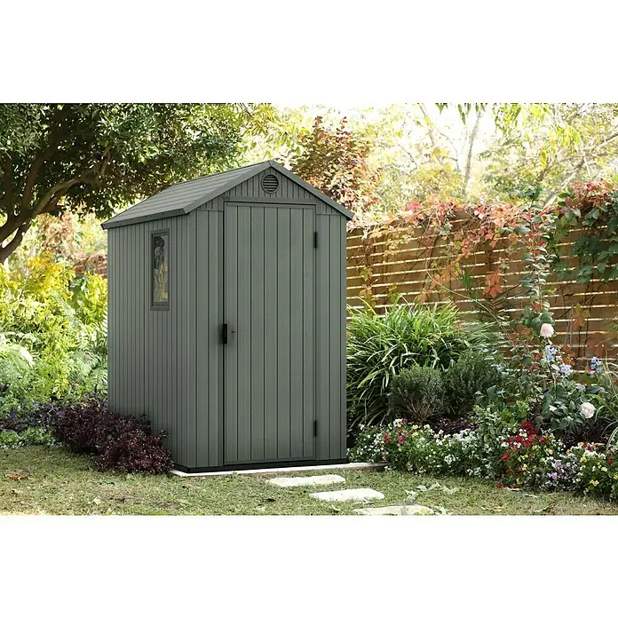 Keter Gerätehaus Darwin 4x6 - Außenmaß inkl. Dachüberstand (B x T): 125,8 x 184,5 cm, Kunststoff, Grün - Ein graues Gartenhaus steht im Garten, umgeben von Blumen und Pflanzen. Das Gartenhaus bietet Stauraum für Gartengeräte.