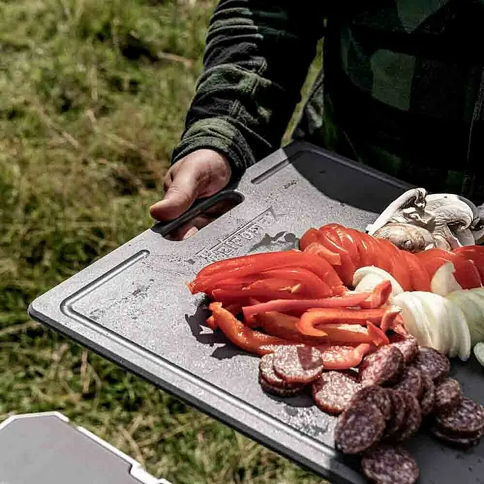 Petromax Schneidebrett - Passend für: Petromax Kühlbox 25l, Kunststoff - Auf einem grauen Schneidebrett liegen Wurstscheiben, Paprika, Zwiebeln und Pilze bereit für die Zubereitung.