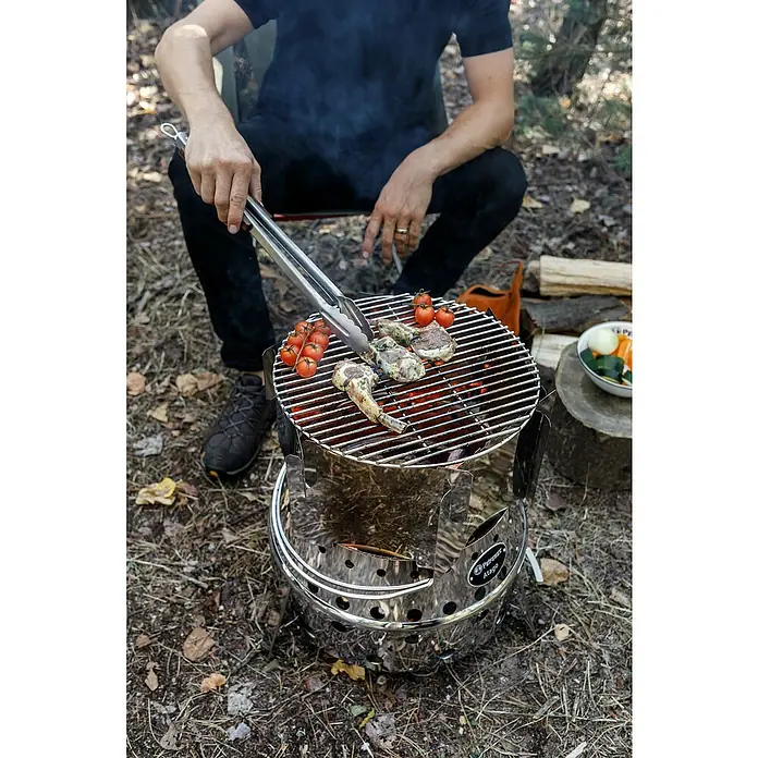 Petromax Grillaufsatz Atago - Passend für: Petromax Grillserie Atago, Edelstahl - Mann grillt mit dem Petromax Atago Fleisch und Gemüse im Freien, ideal für Camping und Outdoor-Abenteuer.