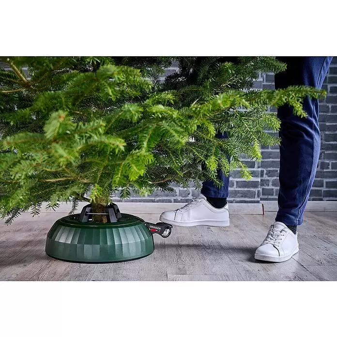 Krinner Christbaumständer X-280 Deluxe - 37 x 11,5 cm, Kunststoff, Rund - Dunkelgrüner Christbaumständer aus Kunststoff hält einen Baum, ein Fuß bedient das Befestigungspedal.