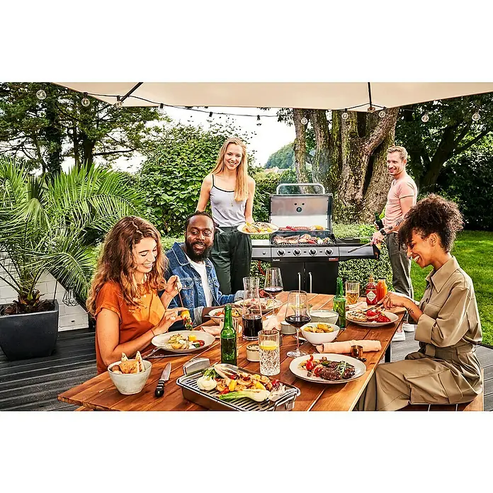 Char-Broil Gasgrill Performance Core B4 - Grillfläche (B x T): 63 x 43,5 cm, 8,68 kW, Anzahl Brenner: 4 - Eine Gruppe von Freunden genießt eine Grillparty im Freien, mit einem Char-Broil-Grill im Hintergrund, der köstliche Speisen zubereitet.