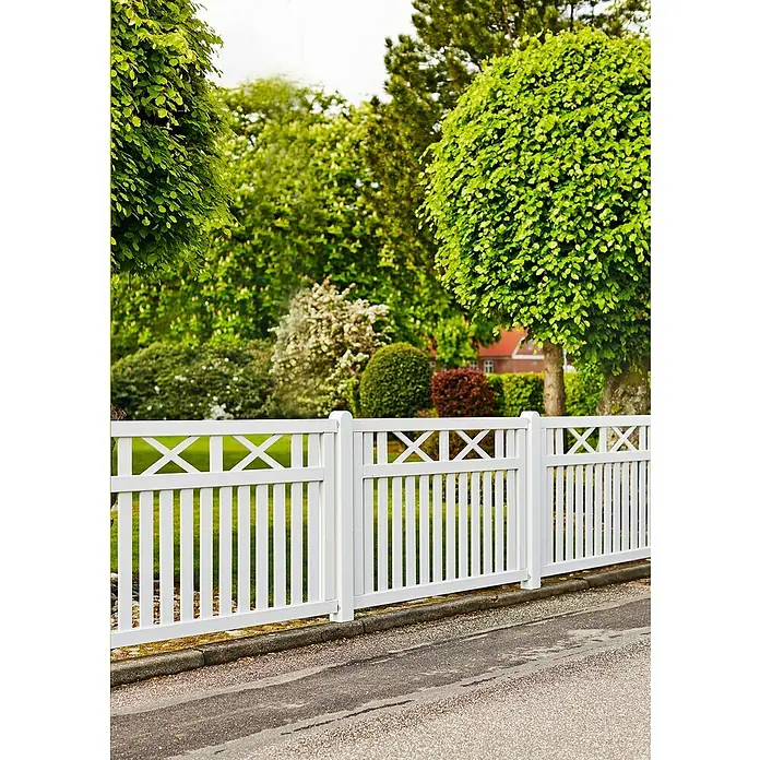 Plus Sichtschutzelement Vinesse - 150 x 96 cm, Holz, Weiß RAL 9010 - Blick auf einen weißen Gartenzaun mit X-förmigen Zierelementen, der einen Garten von einer Straße abgrenzt, umgeben von üppigem Grün.