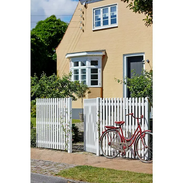 Plus Vorgartenzaun Retro - 150 x 120 cm - Dieses Bild zeigt ein charmantes rotes Fahrrad vor einem weißen Lattenzaun, der ein gelbes Haus ergänzt. Es fängt eine malerische Szene ein.