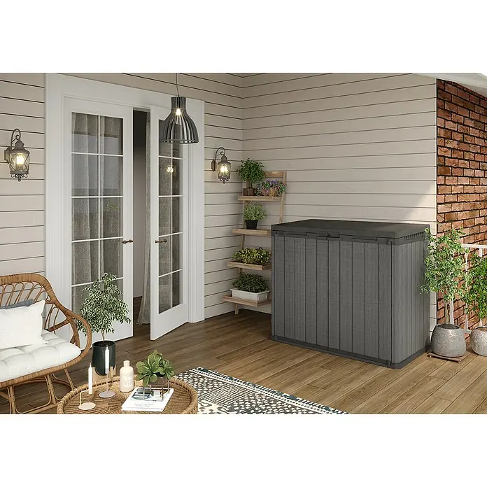 Keter Truhe Store it out Darwin - L x B x H: 80 x 140 x 118 cm, Grau, Kunststoff - Eine graue Gartenbox steht auf einer Holzterrasse, ideal für die Aufbewahrung von Gartengeräten und Kissen.