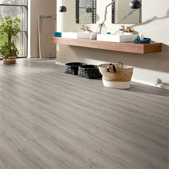 Vinylboden Strong SPC Structure - Carolina, Landhausdiele, 1.220 x 228 x 3,8 mm - Badezimmer mit hellgrauem Vinylboden in Holzoptik, Waschbecken mit Holzablage und geflochtenen Körben.