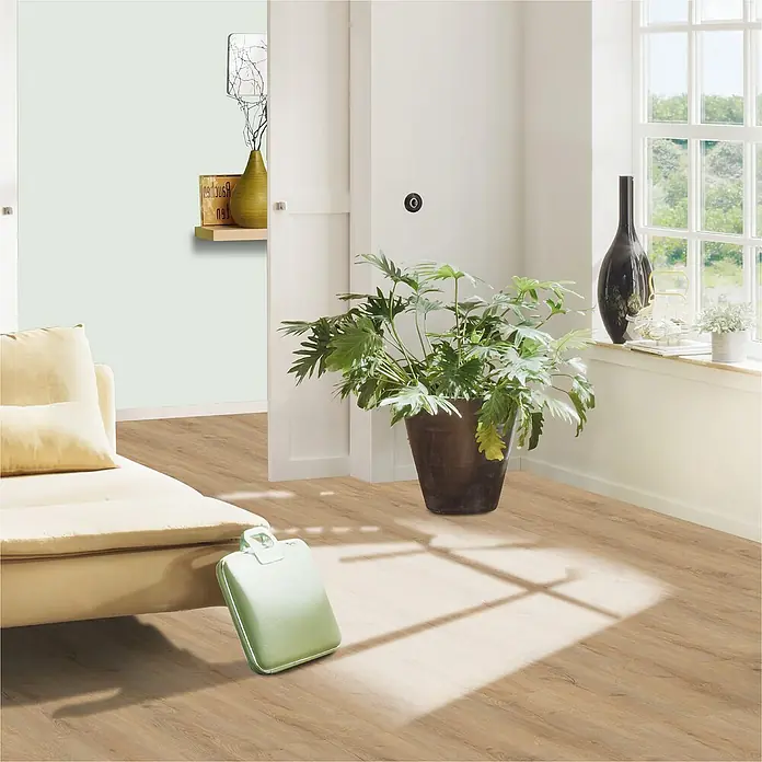 Vinylboden Strong SPC Structure Georgia1.220 x 228 x 3,8 mm, Landhausdiele, Georgia - Das Bild zeigt einen hellen Raum mit einem Laminatboden, einer Pflanze und einem beigen Sofa, was eine gemütliche Atmosphäre schafft.