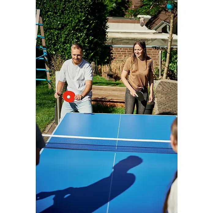 Hudora Tischtennisplatte Match - Blau - Zwei Personen spielen Tischtennis im Freien an einem blauen Tischtennistisch. Sie halten Schläger in der Hand und sind bereit für das Spiel.