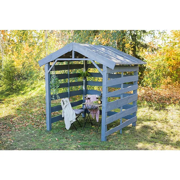 Kaminholzregal Nevada II - 180 x 90 x 220 cm, Holz, Grau - Eine charmante graue Holzlaube mit Tisch und Stühlen, dekoriert mit Pflanzen und einer Decke, lädt zum Verweilen im Garten ein.
