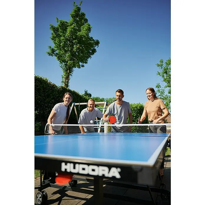 Hudora Tischtennisplatte Match - Blau - Vier Personen spielen Tischtennis auf einer blauen Hudora Tischtennisplatte im Freien.