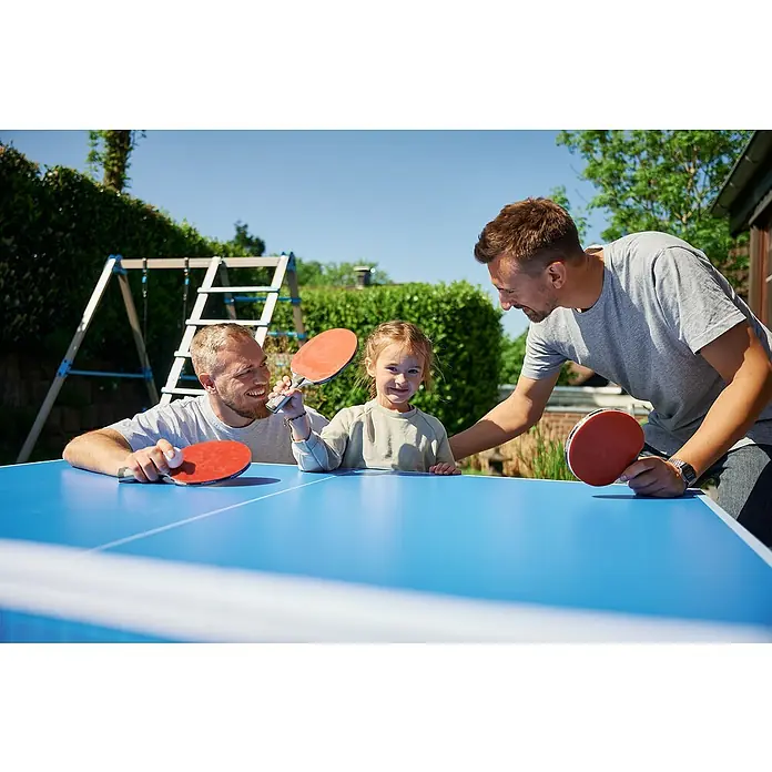 Hudora Tischtennisplatte Match - Blau - Zwei Väter und ihre Tochter spielen Tischtennis im Freien mit roten Schlägern auf einem blauen Tisch. Der Tisch ist der Hauptfokus.