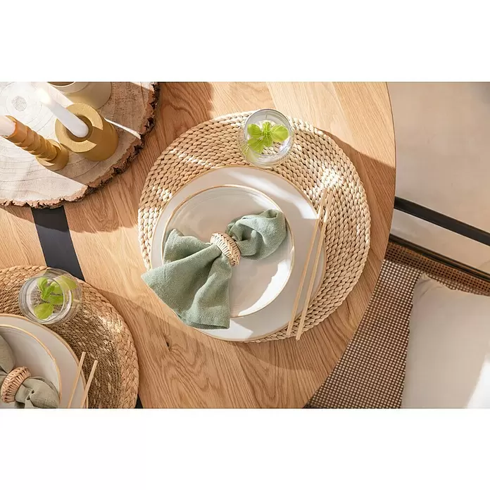 Tisch-Set - Durchmesser: 38 cm, Natur - Ein heller Holztisch, gedeckt mit einem geflochtenen Platzset, weißen Tellern, einer grünen Serviette mit geflochtenem Ring und Essstäbchen.