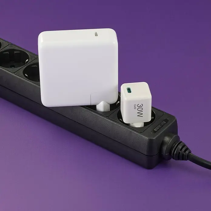 Hama USB-Adapter Schnellladegerät - 30 W, Weiß, USB C-Stecker - Bild von zwei Ladegeräten (einem großen, einem kleinen) an einer schwarzen Steckdosenleiste auf lila Hintergrund.