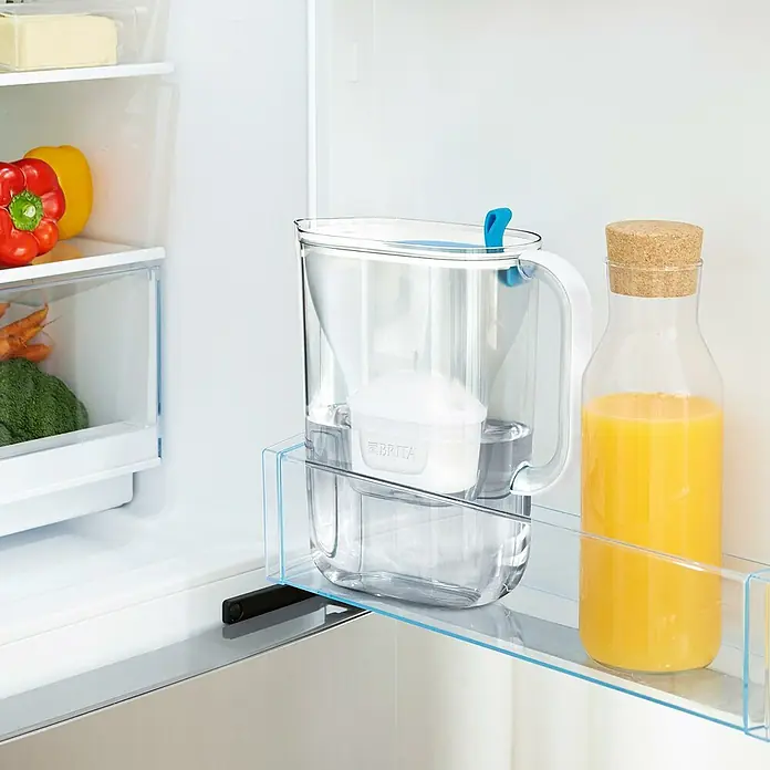 Brita Jarra filtrante Maxtra Pro - Capacidad volumétrica: 2,4 l, 1 ud., Transparente/Azul - Un filtro de agua Brita y una botella de jugo de naranja colocados en un estante de vidrio dentro de un refrigerador. Imagen que muestra opciones de bebidas saludables.