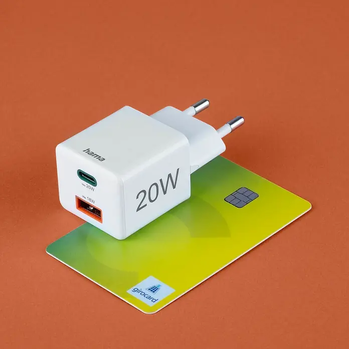 Hama USB-Adapter Schnellladegerät USB-C+A - Weiß, 20 W - Das Bild zeigt ein Hama 20W Ladegerät, das auf einer Girocard liegt. Das Ladegerät ist weiß und hat zwei Anschlüsse, USB-C und USB-A.