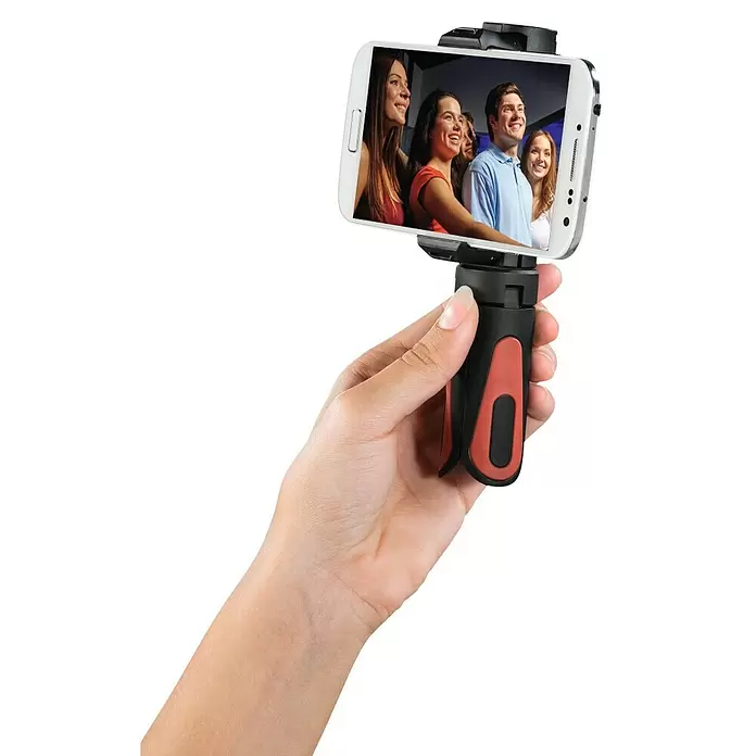 Hama Smartphone-Halter Mini-Stativ "Pocket II Rotation" 15 cm - Schwarz, Rot - Hand hält schwarzen und roten Smartphone-Halter/Mini-Stativ mit Smartphone, das lachende Menschen zeigt.