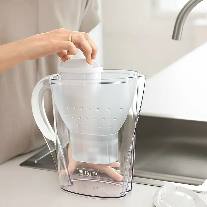 Brita Jarra filtrante Marella - Capacidad volumétrica: 2,4 l, 1 ud., Transparente/Blanco - Primer plano de una persona colocando un filtro de agua Brita blanco en una jarra Brita transparente sobre una encimera de cocina.