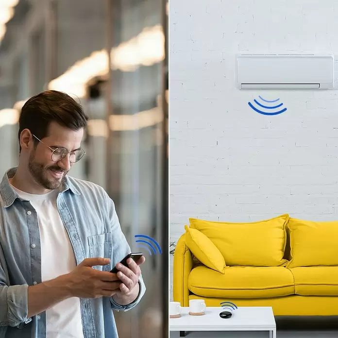 Hama Wifi Steuerzentrale WLAN-Universal-Fernbedienung Infrarot für Sprach- / App-Steuerung - Schwarz - Mann steuert Klimaanlage fern mit Smartphone und schwarzer Smart-IR-Fernbedienung auf weißem Tisch im Wohnzimmer.