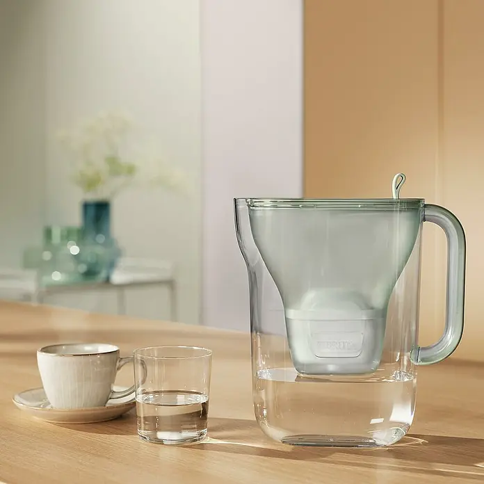 Brita Cartucho para jarra filtrante Maxtra Pro Experto en Cal - Específico para: Jarras filtrantes Brita, 4 pzs. - Jarra de filtro de agua Brita sobre una mesa con taza y vaso. La jarra está llena de agua y lista para filtrar.