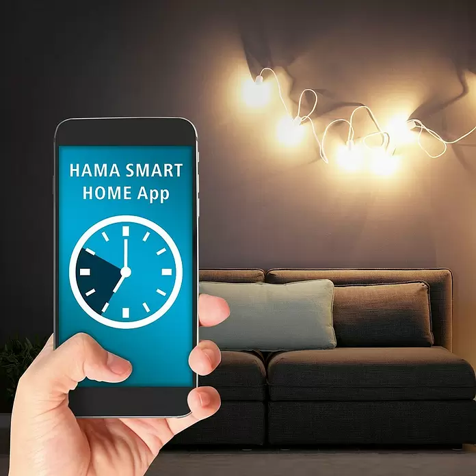 Hama Wifi Smart-LED-Lampe Filament - E27, Dimmbar, RGBW, 470 lm, 4,9 W - Smartphone zeigt HAMA SMART HOME App mit Timer, in einer Hand gehalten, in Wohnzimmer mit Lichterkette.