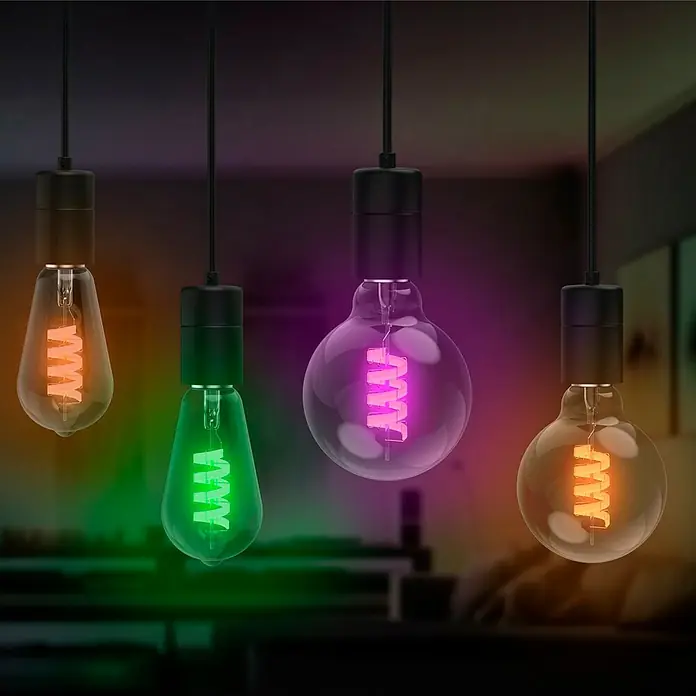 Hama Wifi Smart-LED-Lampe Filament Matter - E27, Dimmbar, RGBW, 470 lm, 4,9 W - Eine Nahaufnahme von vier intelligenten Glühbirnen in verschiedenen Farben, die an Kabeln in einem dunklen Raum hängen.