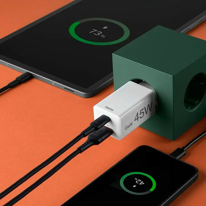 Hama USB-Adapter Schnellladegerät USB-C+A - Weiß, 45 W - Nahaufnahme eines Hama GaN 45W-Ladegeräts, das in eine grüne Würfelsteckdose eingesteckt ist und ein Tablet und ein Smartphone auflädt.