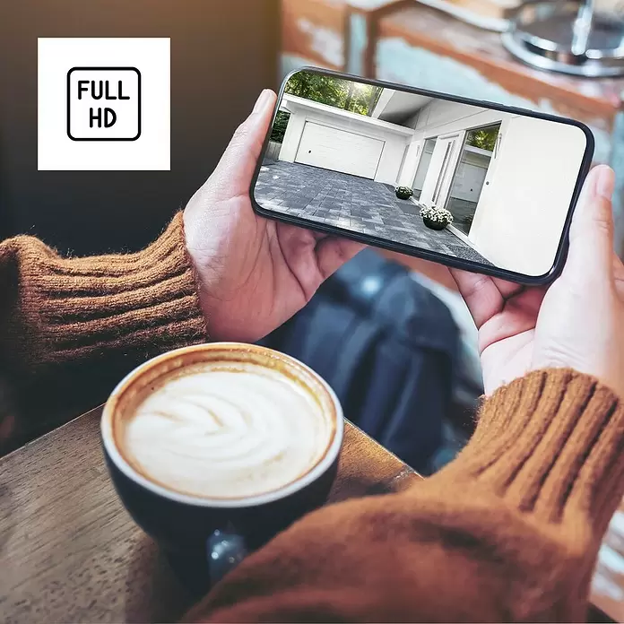 Hama Wifi Überwachungskamera - Weiß, Erfassungswinkel: 110 ° - Hände halten ein Smartphone, das ein modernes weißes Garagentor und einen Hauseingang zeigt, mit einem 'FULL HD'-Symbol als Overlay.