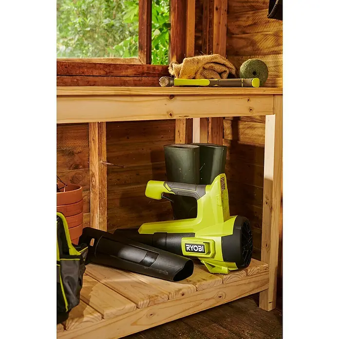 Ryobi ONE+ Akku-Gebläse RY18BLB-0 - 18 V, Ohne Akku, Blasgeschwindigkeit: 160 km/h - Nahaufnahme eines Ryobi Akku-Laubbläsers in einem Holzschuppen, der Gartengeräte beherbergt.